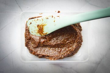 The vegan truffle mix in a plastic container with a spatula on top.