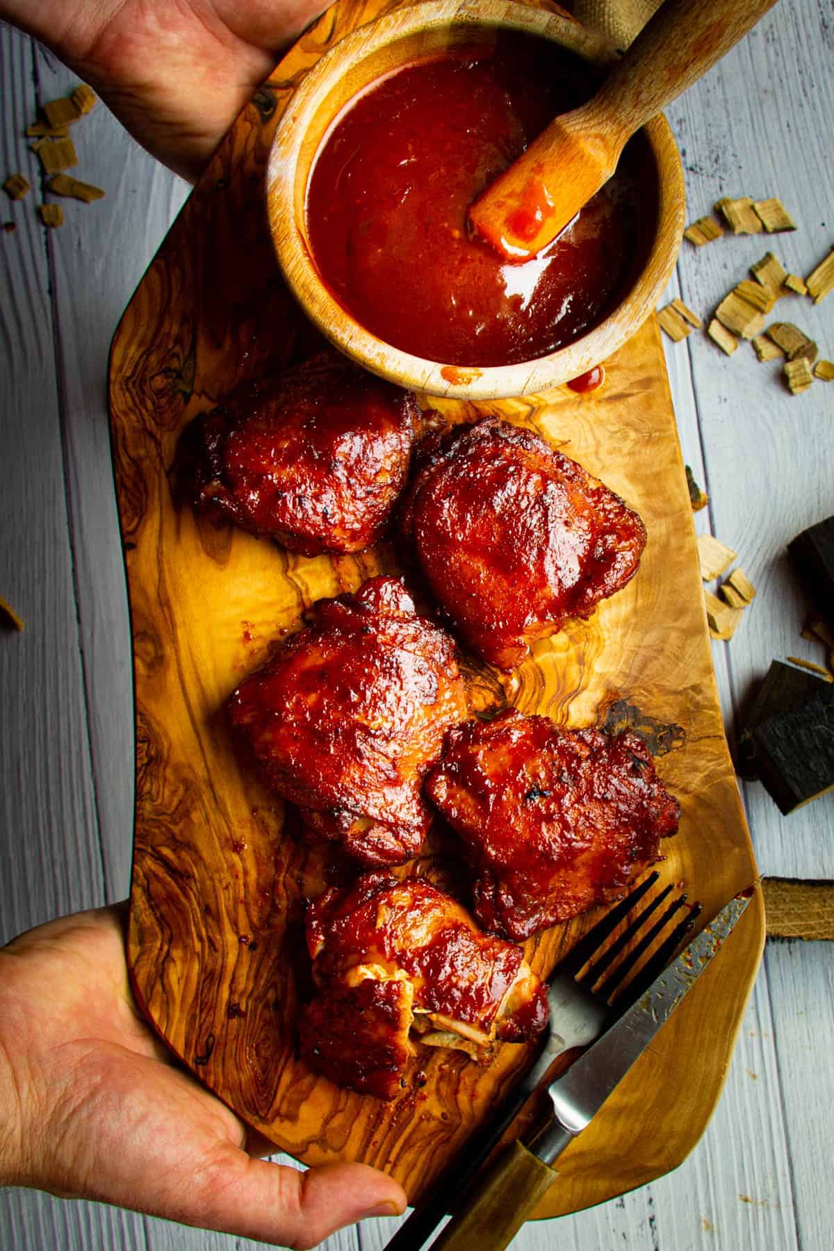 5 smoked chicken thighs on a board with extra bbq sauce on the side.