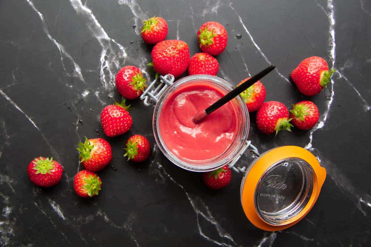 Strawberry puree on a black marble background with fresh strawberries on the side.