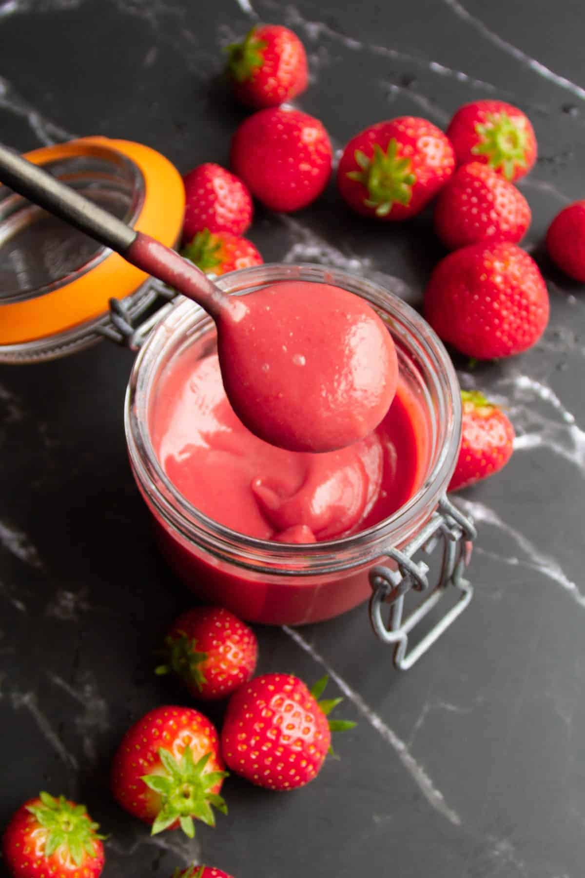 strawberry puree on a spoon over a mason jar