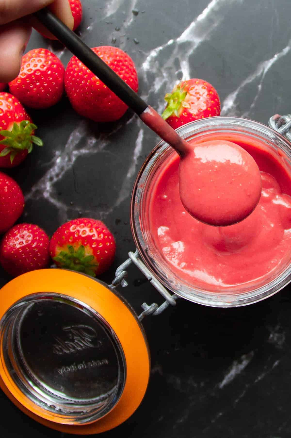 strawberry puree on a spoon over a mason jar