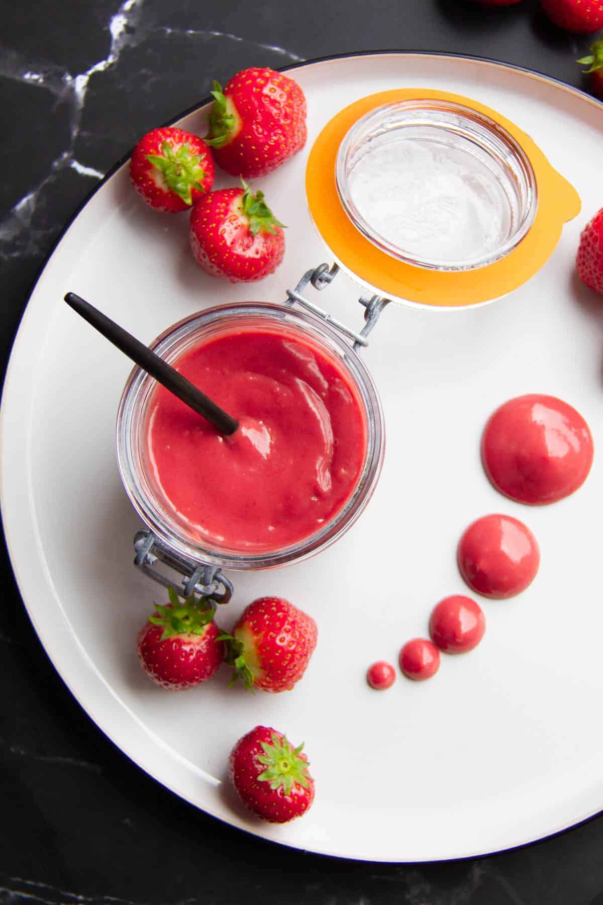 strawberry puree in a mason jar with dots of the puree on the side