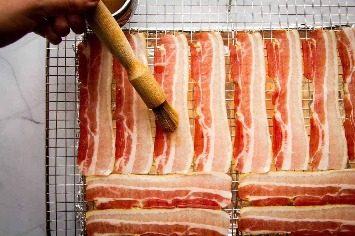 Brushing the bacon with maple syrup.