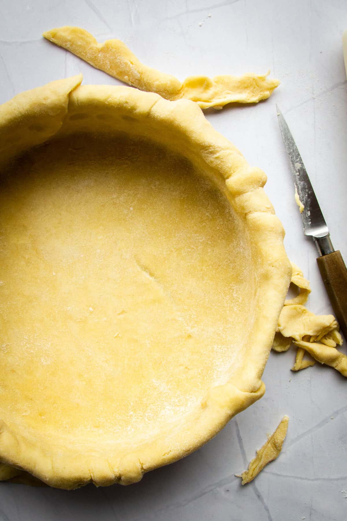 A pie crust rolled into a pie tray with a knife and some pie trim on the side.