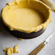 A pie crust rolled into a pie tray with a knife and some pie trim on the side.