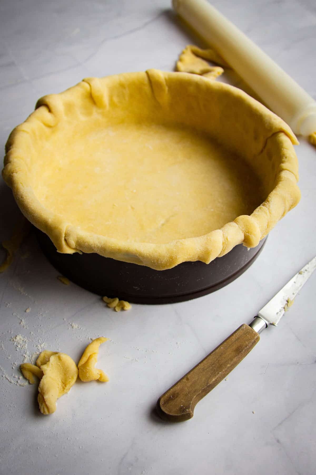 A pie crust rolled into a pie tray with a knife and some pie trim on the side.