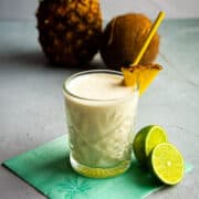 A pina colada on the table with fresh pinapple and coconut in the back.