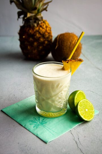 A pina colada on the table with fresh pinapple and coconut in the back.