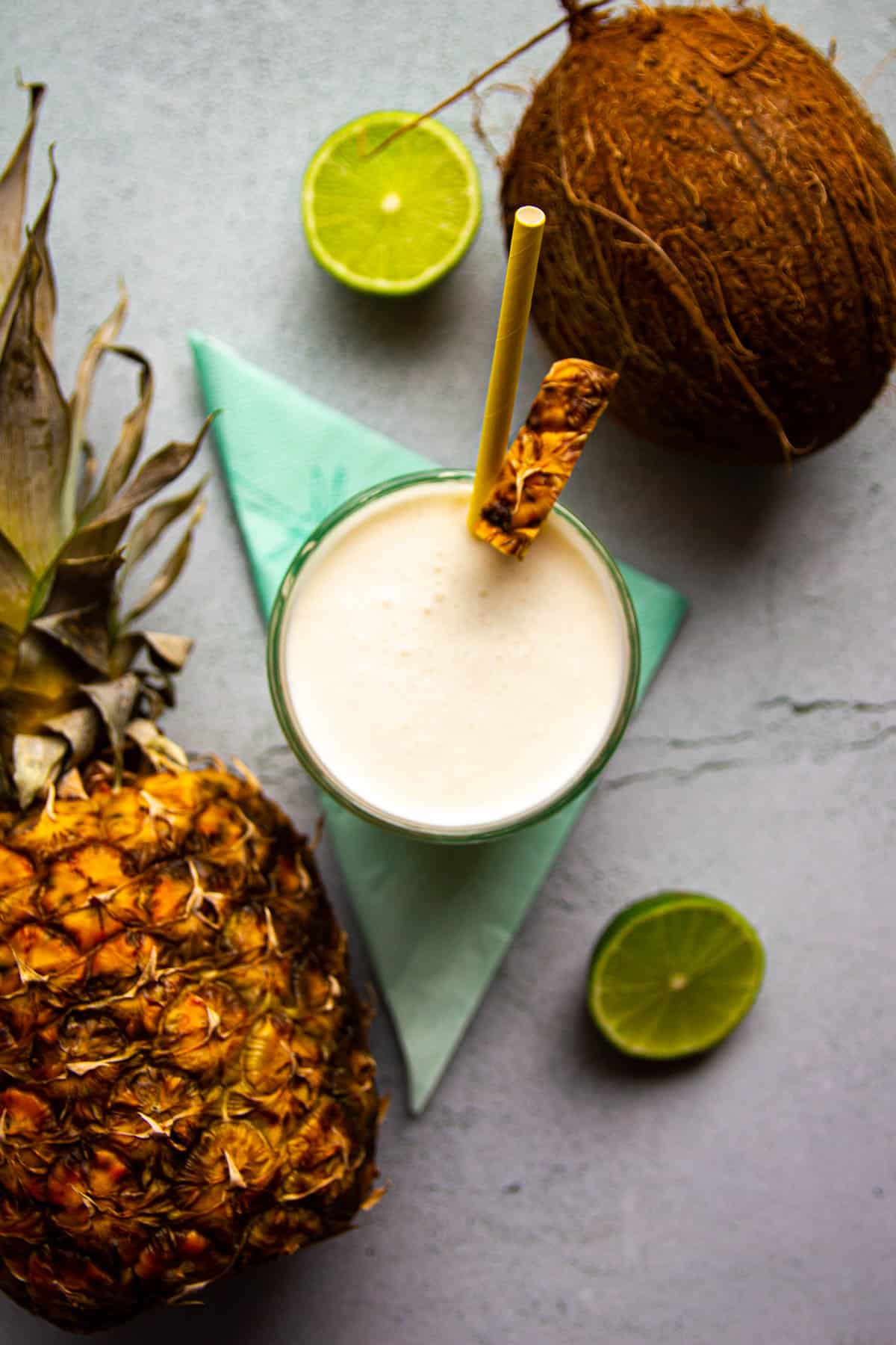 A pina colada on the table with fresh pinapple and coconut in the back.