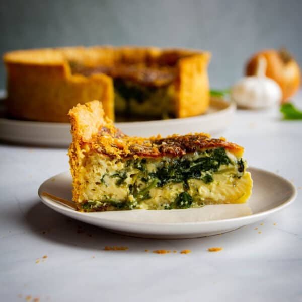 Side angle shot of a slice of quiche florentine with the rest of the quiche in the background.