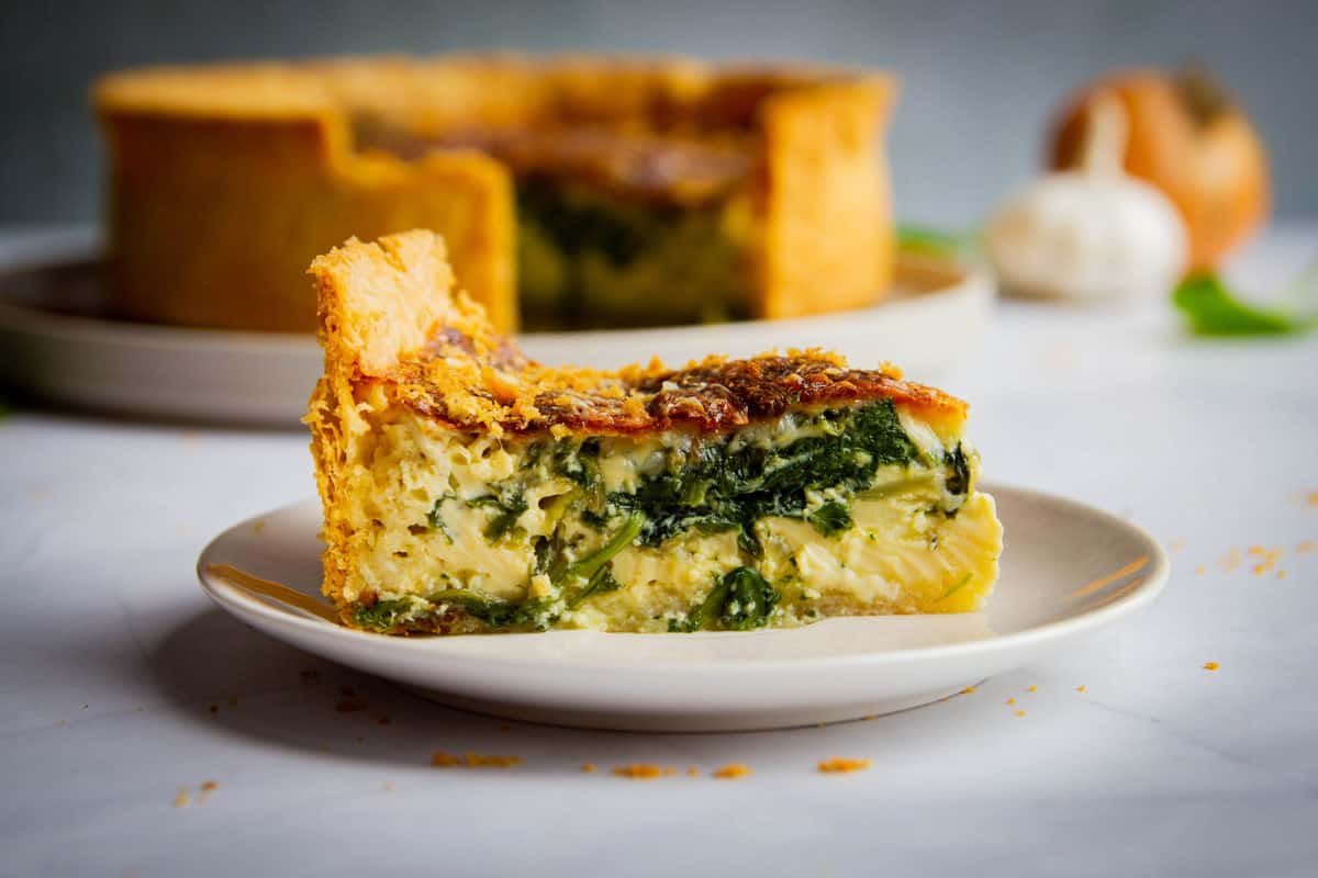 Side angle shot of a slice of quiche florentine with the rest of the quiche in the background.
