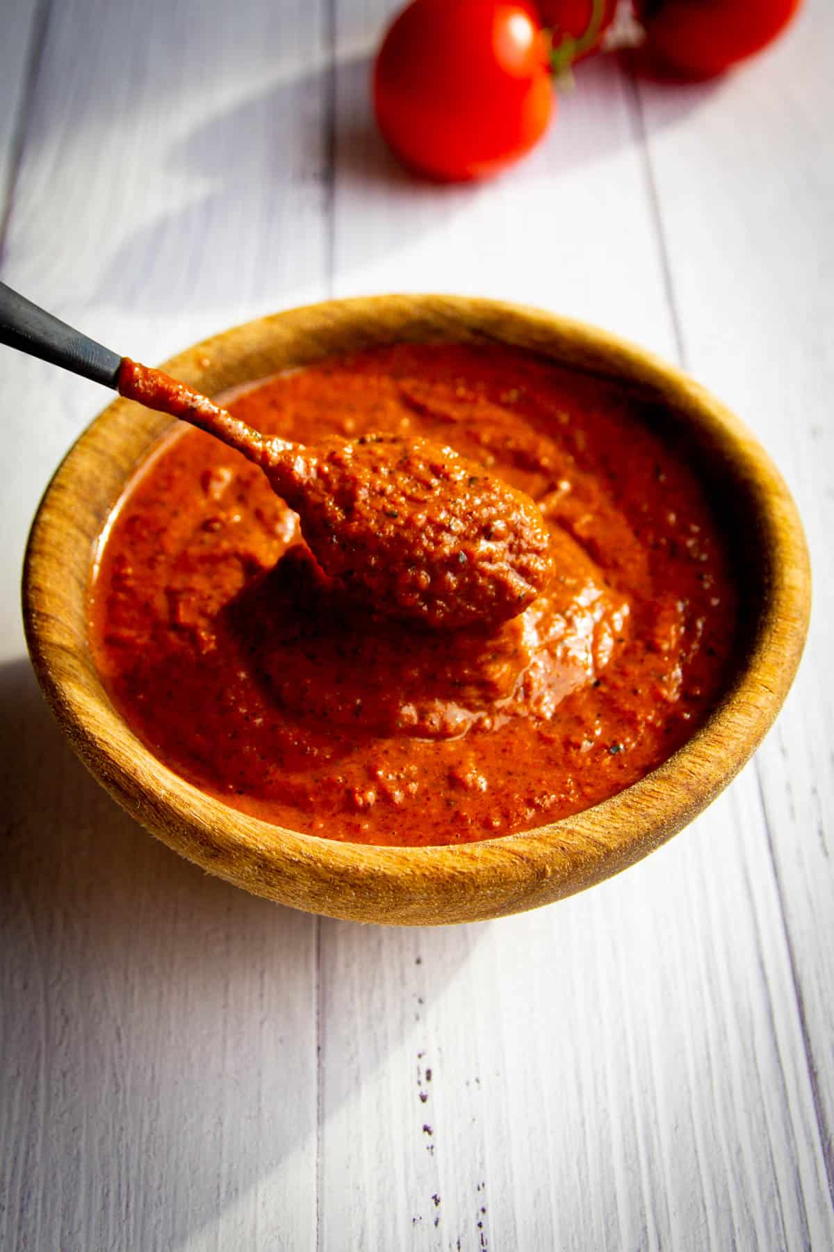 A spoon dipped inside a bowl of roasted cherry tomato salsa.