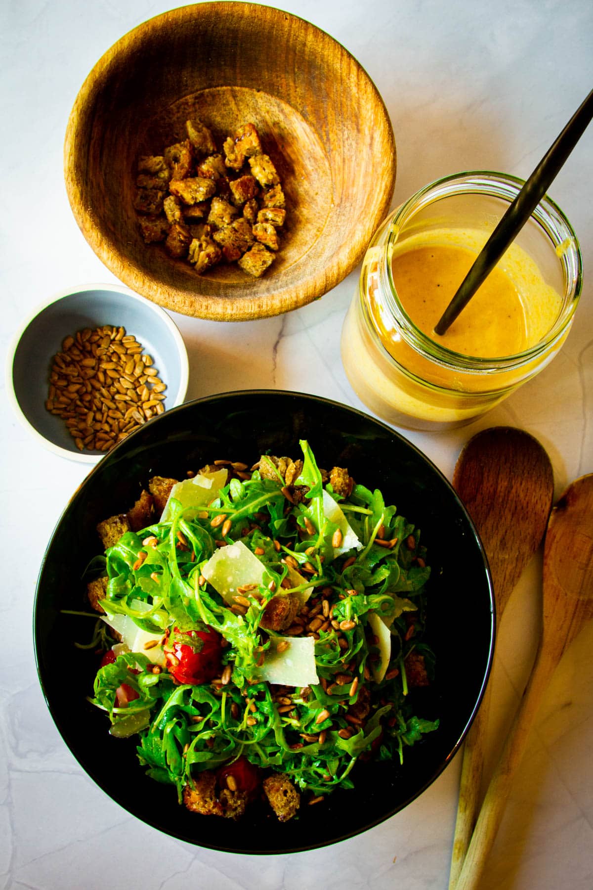 A rocket salad, sunflower dressing, croutons and sunflower seeds on the table.