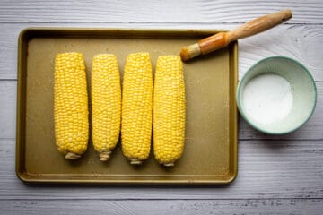 Seasoning the corn cobs with oil and salt.