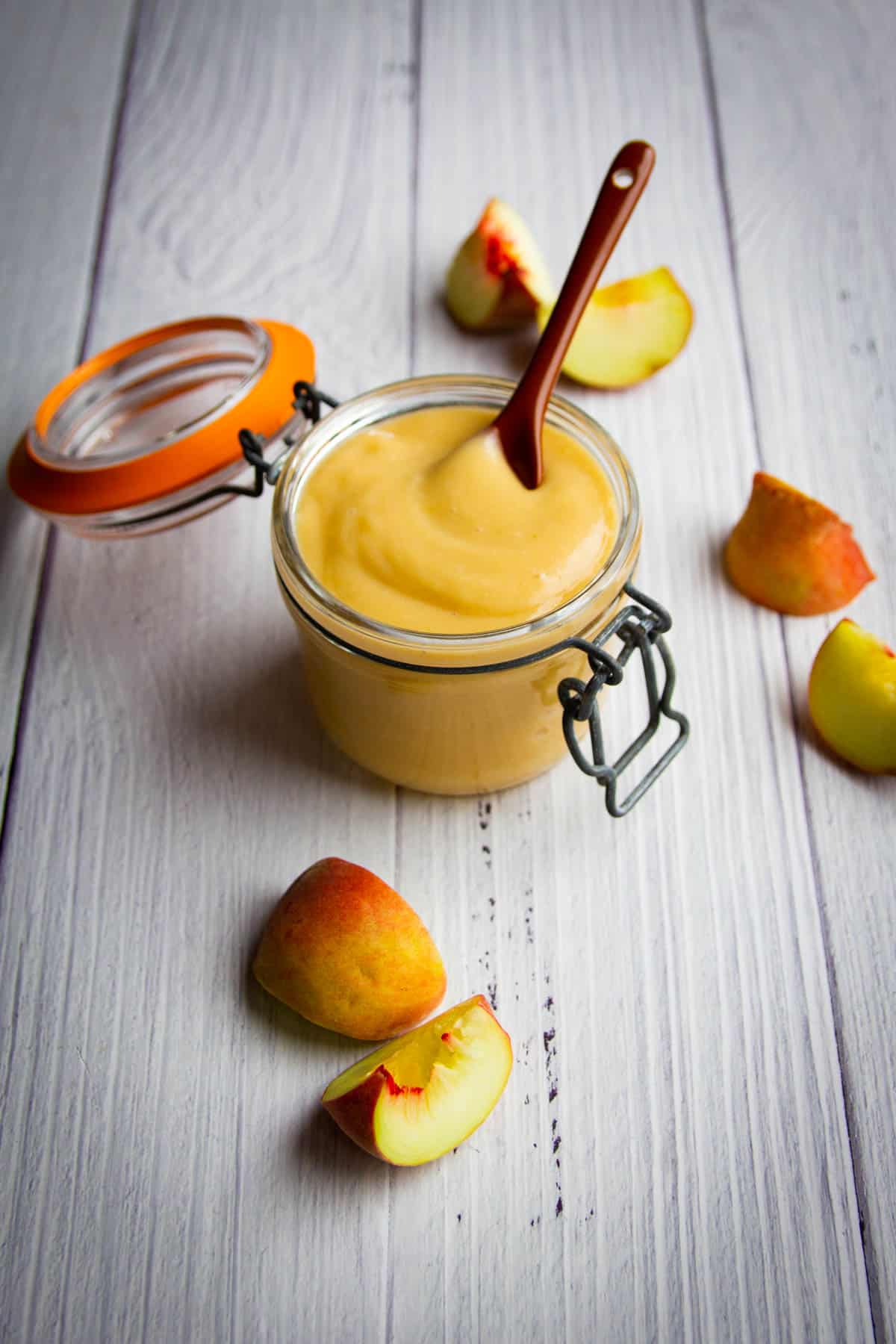 The white peach puree on a spoon with fresh peaches in the background.