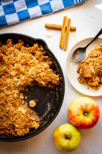 A slice of apple crisp on a plate with the rest of the apple crisp behind