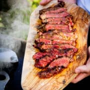 A smoked, reverse-seared ribeye sliced on a wooden board with smoke in the background.