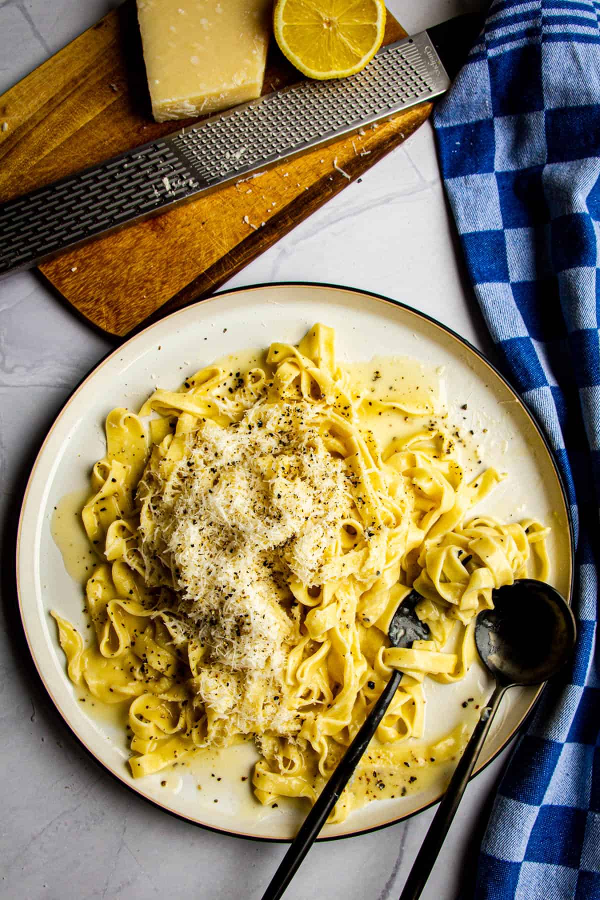 Tagliatelle cacio e pepe on a plate with parmigiano and lemon on the side.