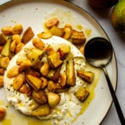 Whole burrata on a plate with roasted pears, thyme, marcona almonds and brown butter