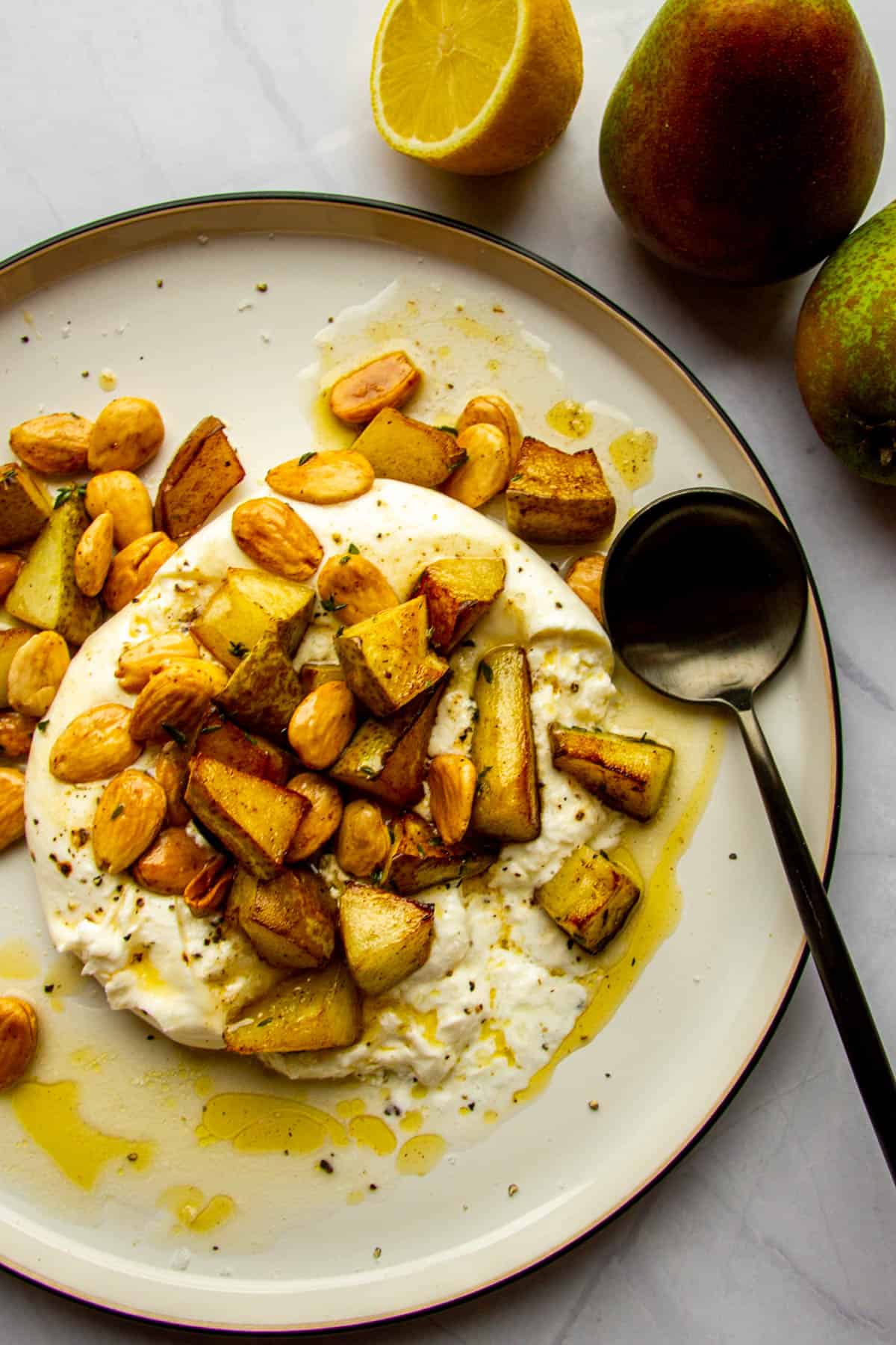 Whole burrata on a plate with roasted pears, thyme, marcona almonds and brown butter