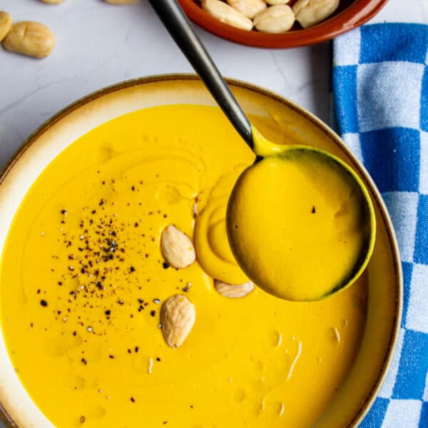Red Kuri Squash soup in a bowl with toasted marcona almonds on top and a spoon inside.