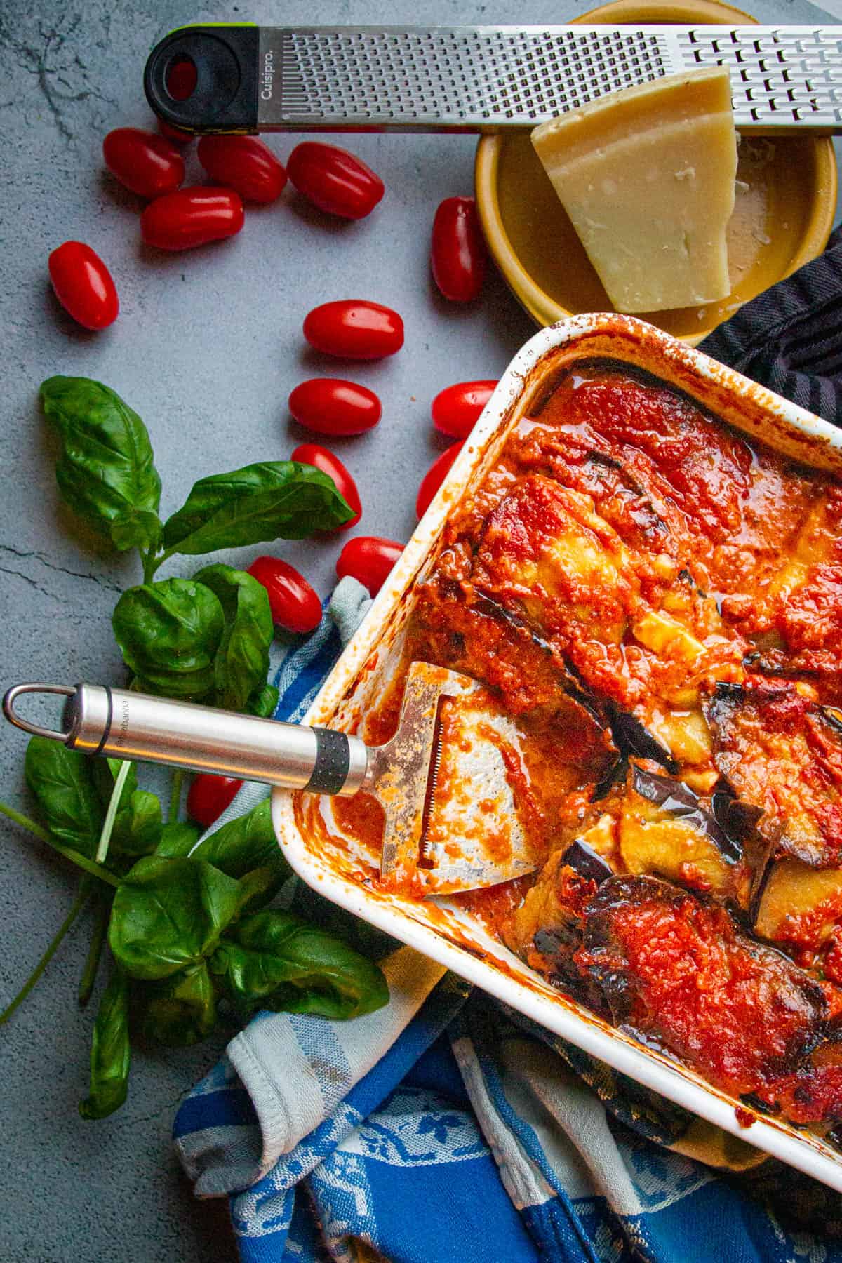 Keto eggplant parm on a table with tomatoes basil and cheese on the side.