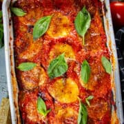 Keto eggplant parmesan on a table with tomatoes and cheese around.