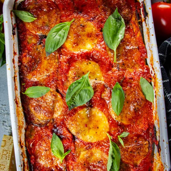 Keto eggplant parmesan on a table with tomatoes and cheese around.