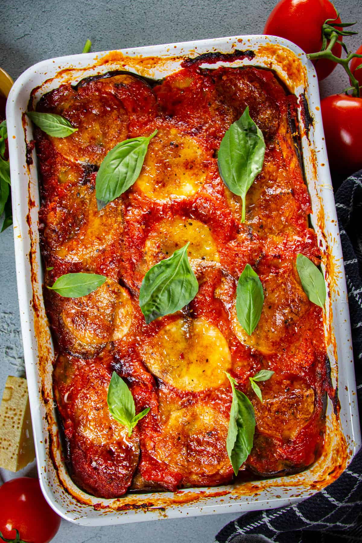 Keto eggplant parmesan on a table with tomatoes and cheese around.