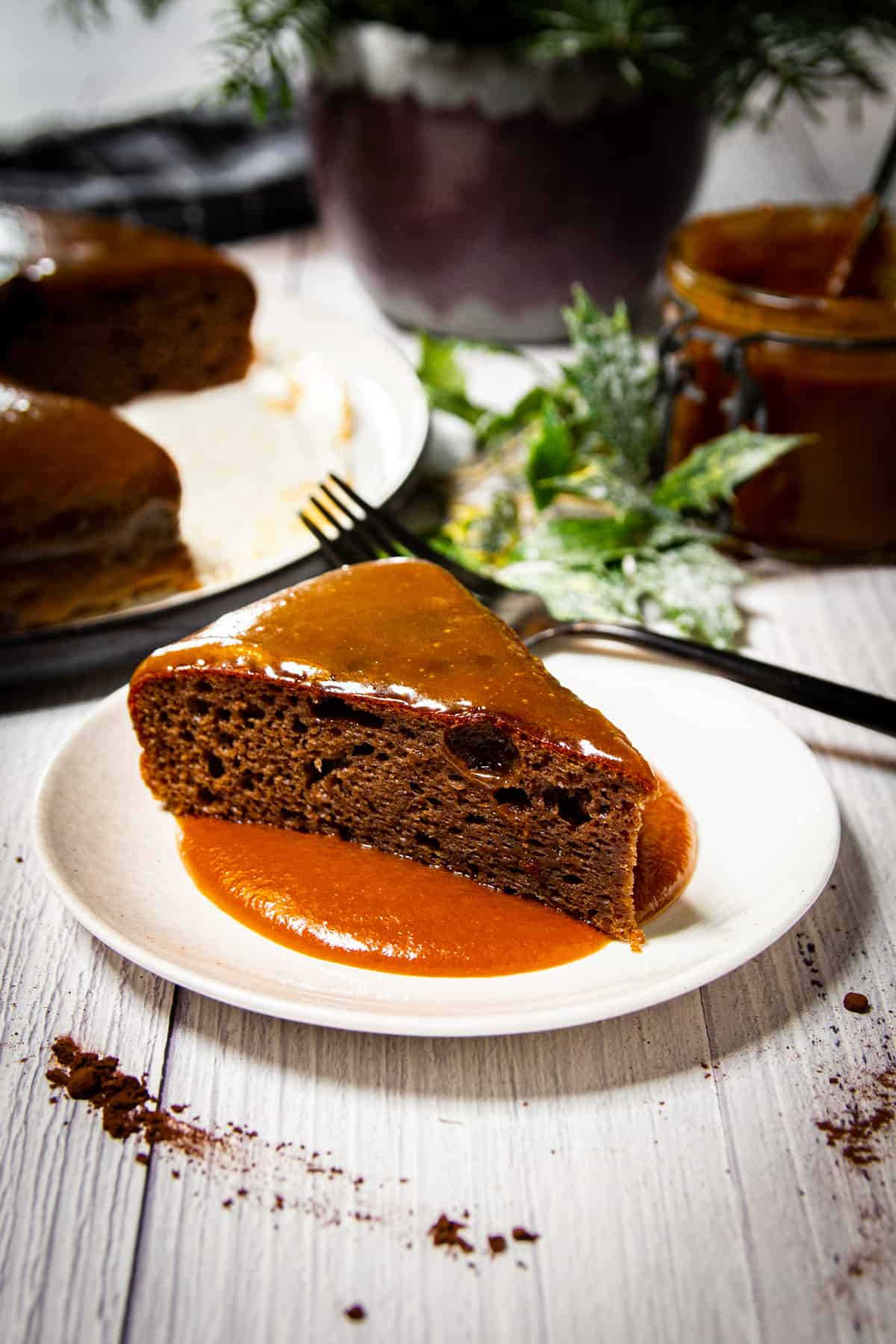 A slice of the sticky toffee pudding with the full cake and some christmas decorations in the background.