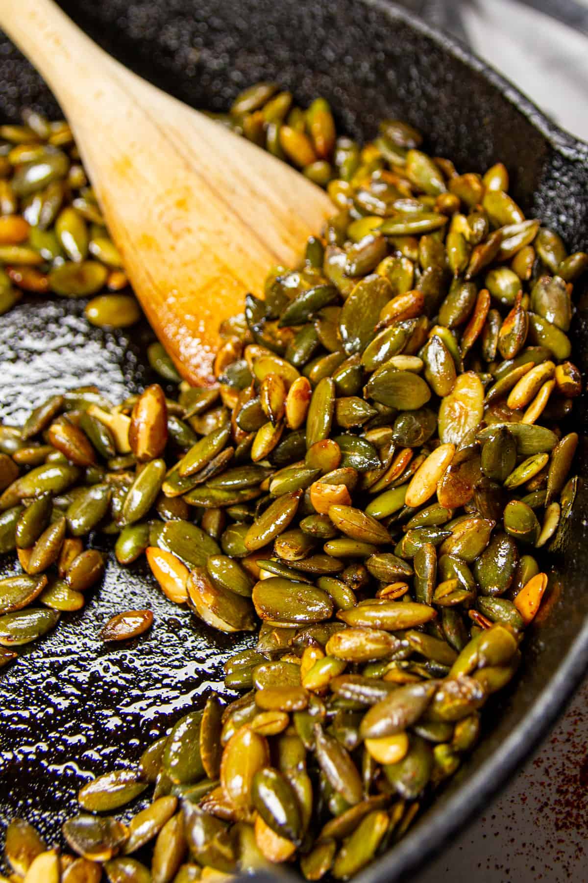 Roasted pepitas in chicken fat, chili and cinnamon in a cast iron pan with a wooden spoon.