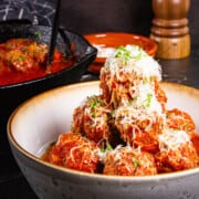 Meatballs without breadcrumbs stacked high in a bowl and covered with parmigiano cheese.