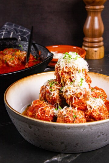 Meatballs without breadcrumbs stacked high in a bowl and covered with parmigiano cheese.