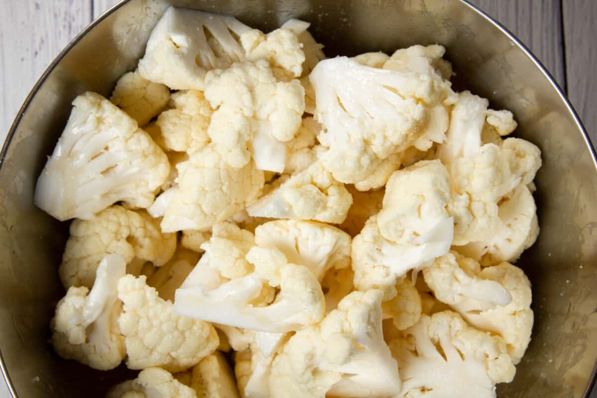 Tossing the cauliflower in a bowl with oil and salt.