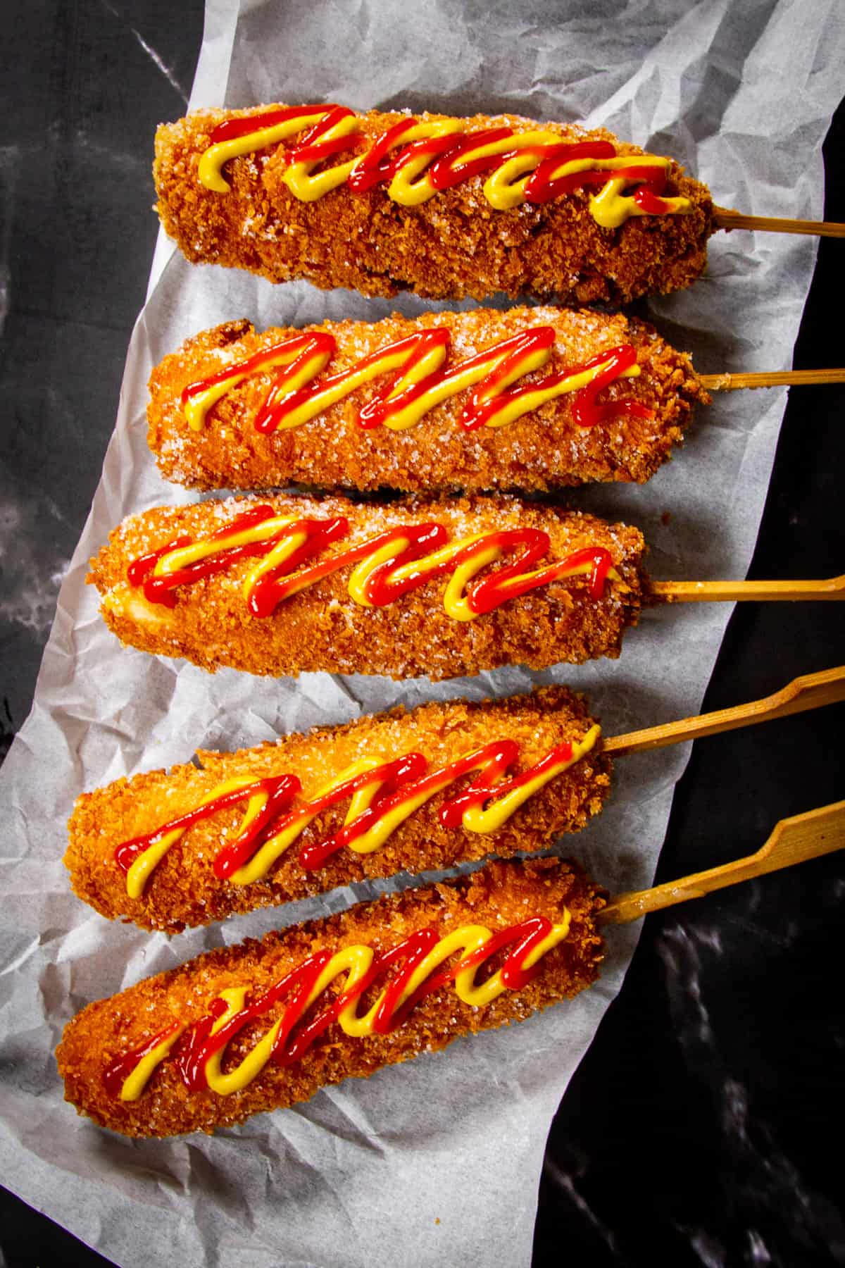 5 Korean corn dogs with ketchup and mustard on a black marble table.