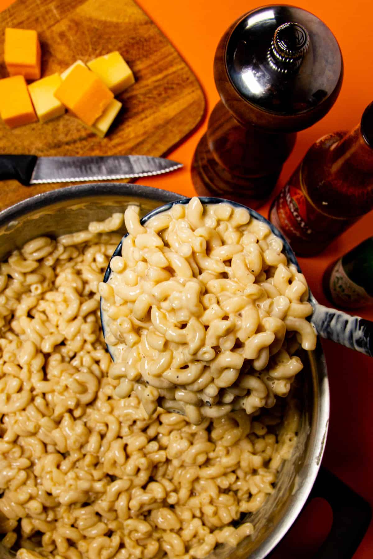 Macaroni and cheese in a giant ladle with a pepper shaker and cheddar cheese in the background.