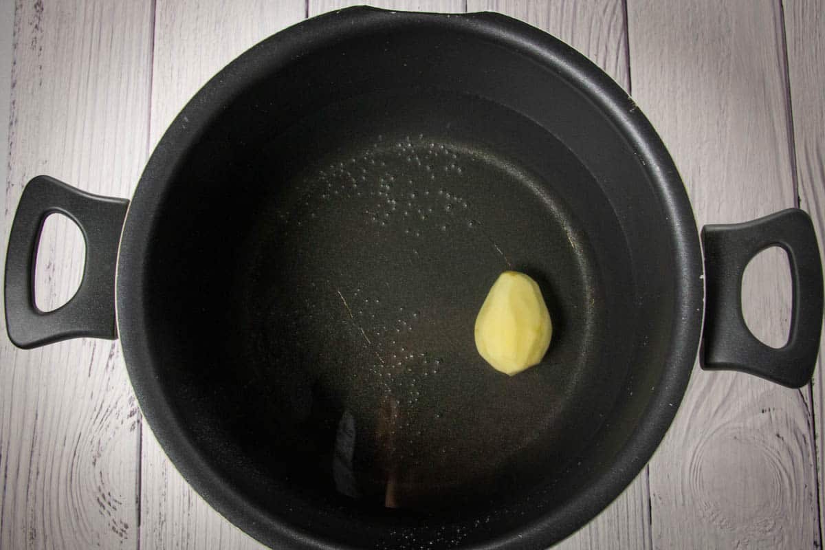 A small peeled potato in a large pasta pot.