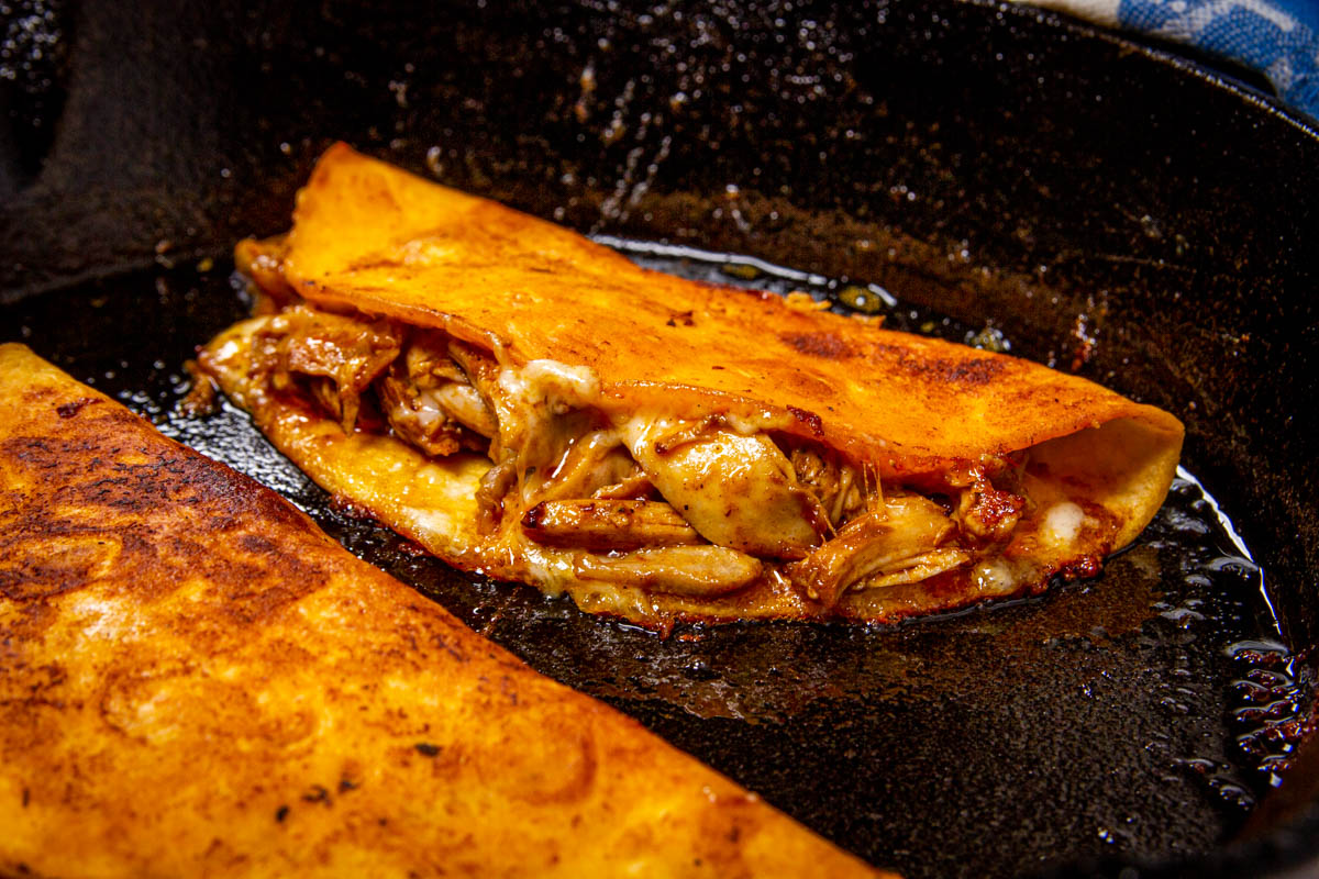 Frying the chicken birria tacos in a cast iron pan.