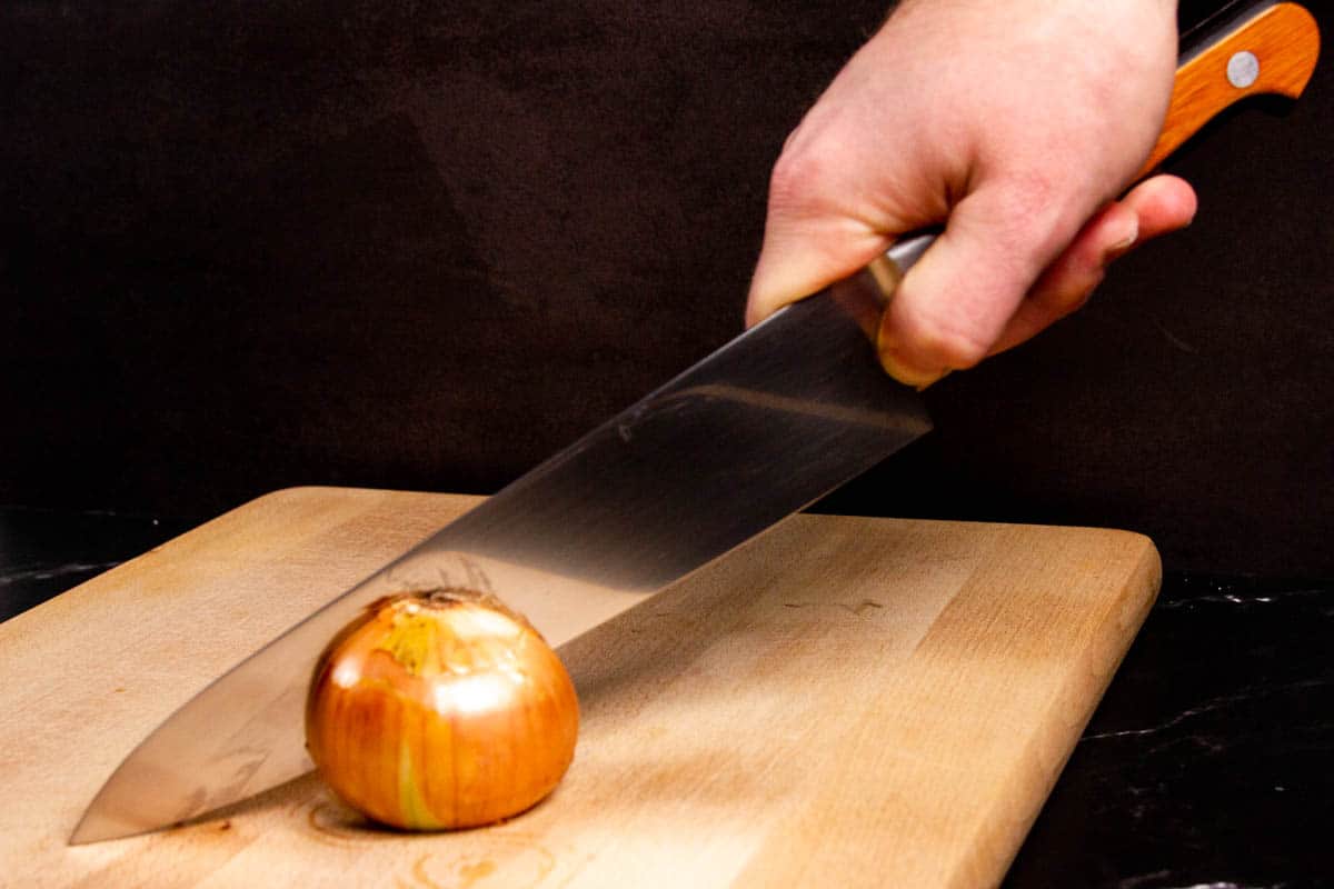 Slicing an onion in half on a cutting board with a suisin chef knife.