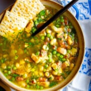 A navy bean soup cooked in an Instant pot in a bowl with a spoon and crackers dipped inside.