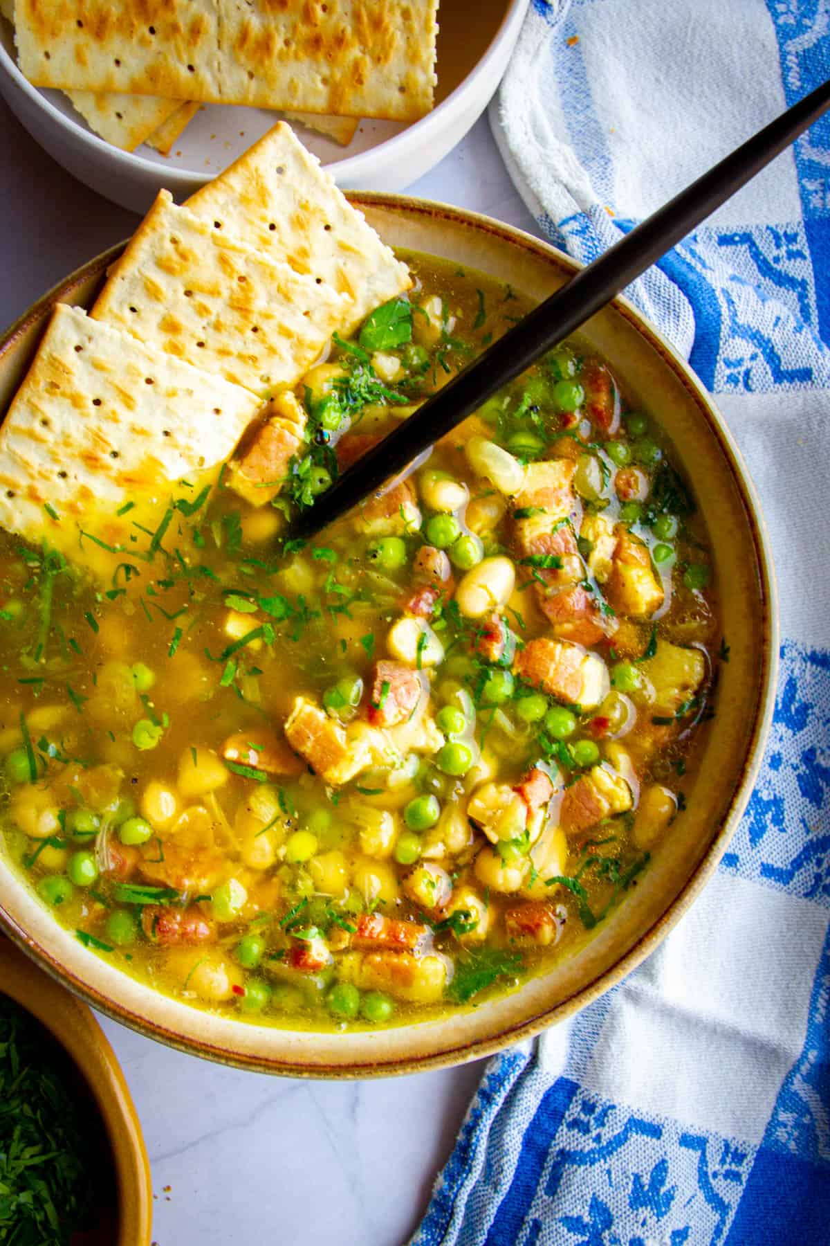 A navy bean soup cooked in an Instant pot in a bowl with a spoon and crackers dipped inside.