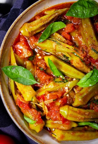 Frozen okra (bamia) in a bowl with basil leaves and tomato.