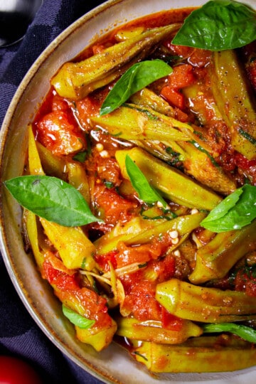 Frozen okra (bamia) in a bowl with basil leaves and tomato.