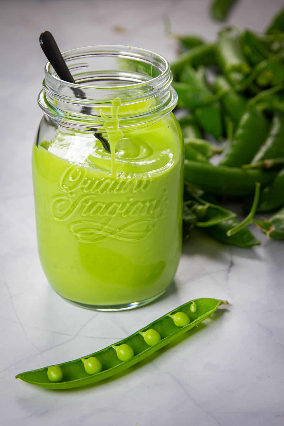 A mason jar full of pea puree with fresh peas beside it.