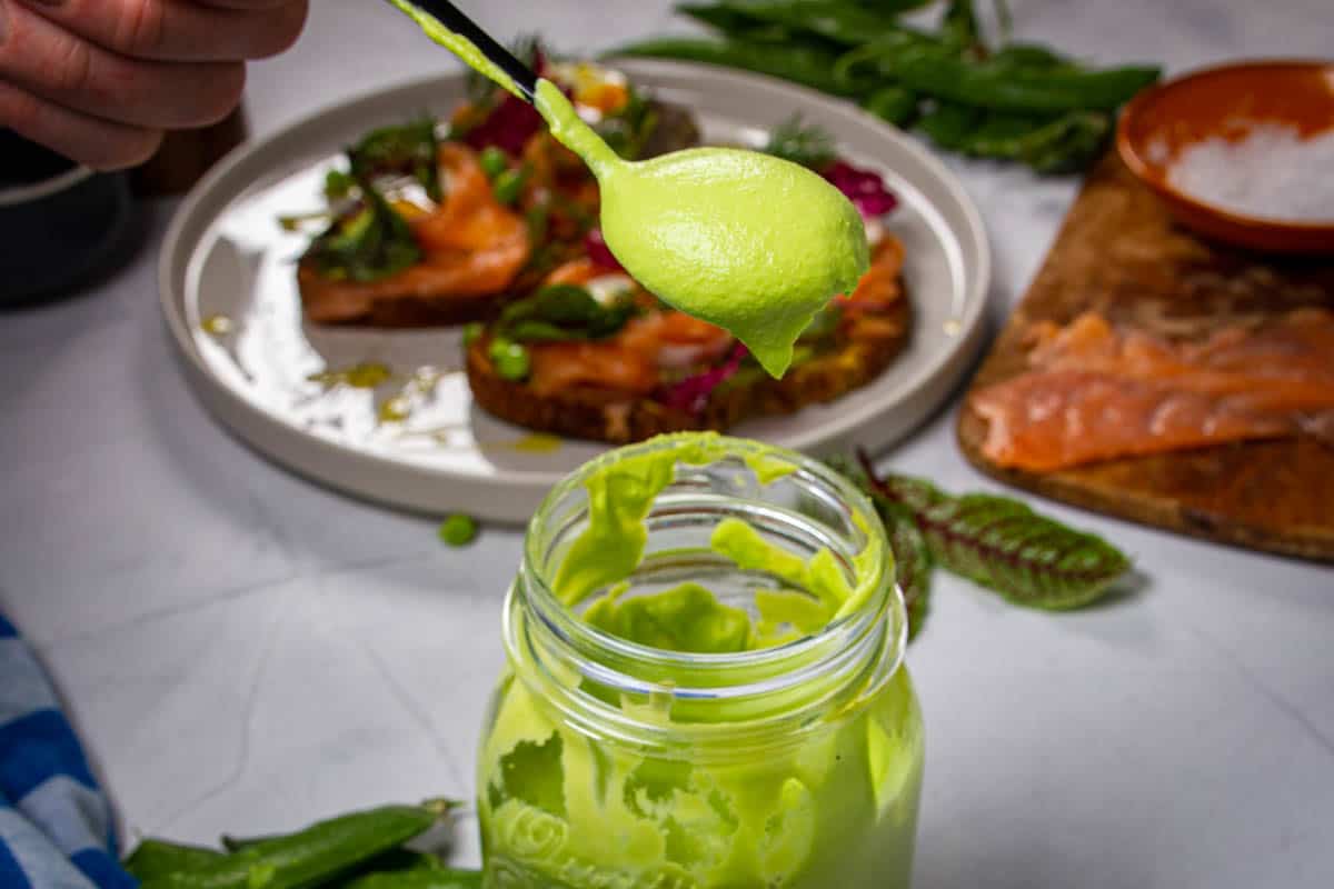 A spoon of pea puree held over the jar.
