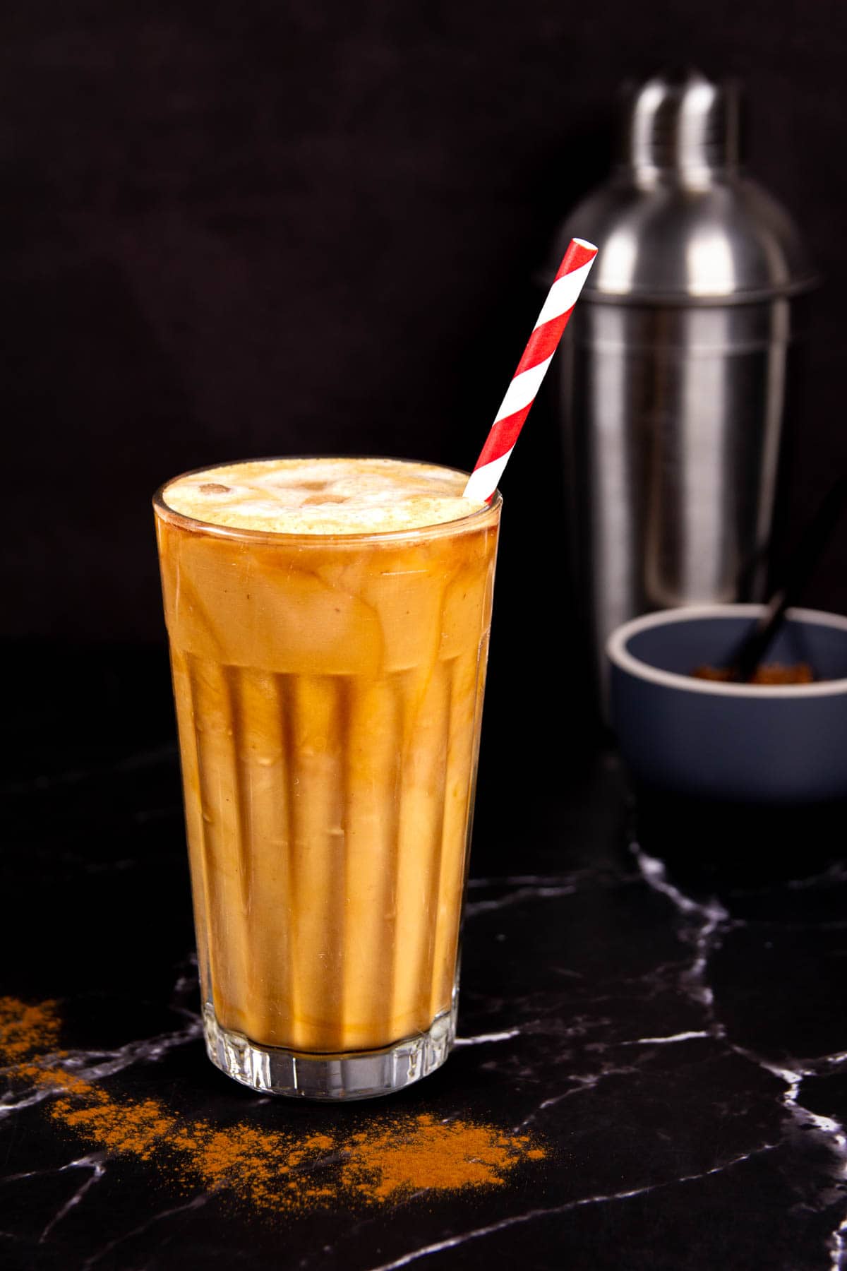 A frothy Brown Sugar Oatmilk Shaken Espresso in a tall glass with a striped paper straw.
