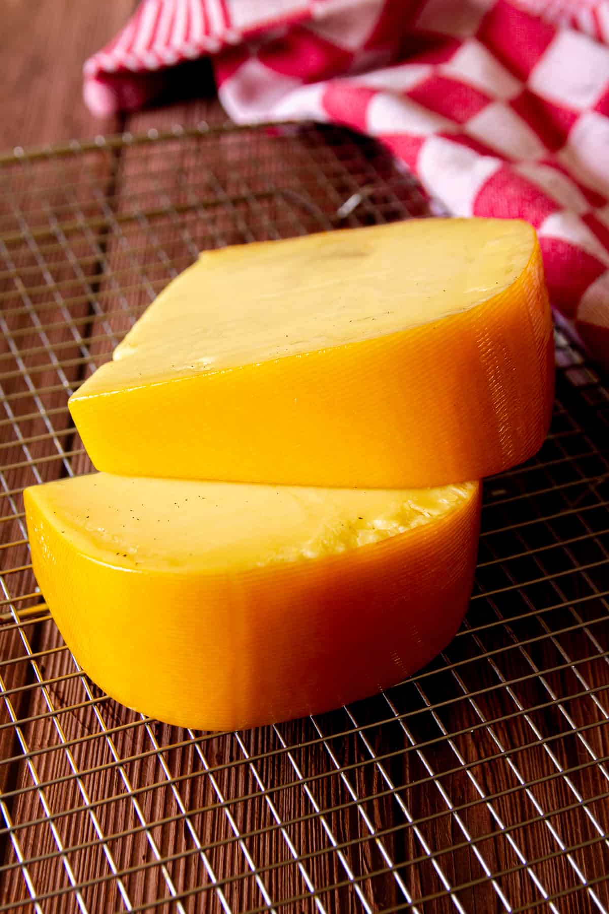 Two large pieces of smoked gouda on a wire rack with a red towel in the background.