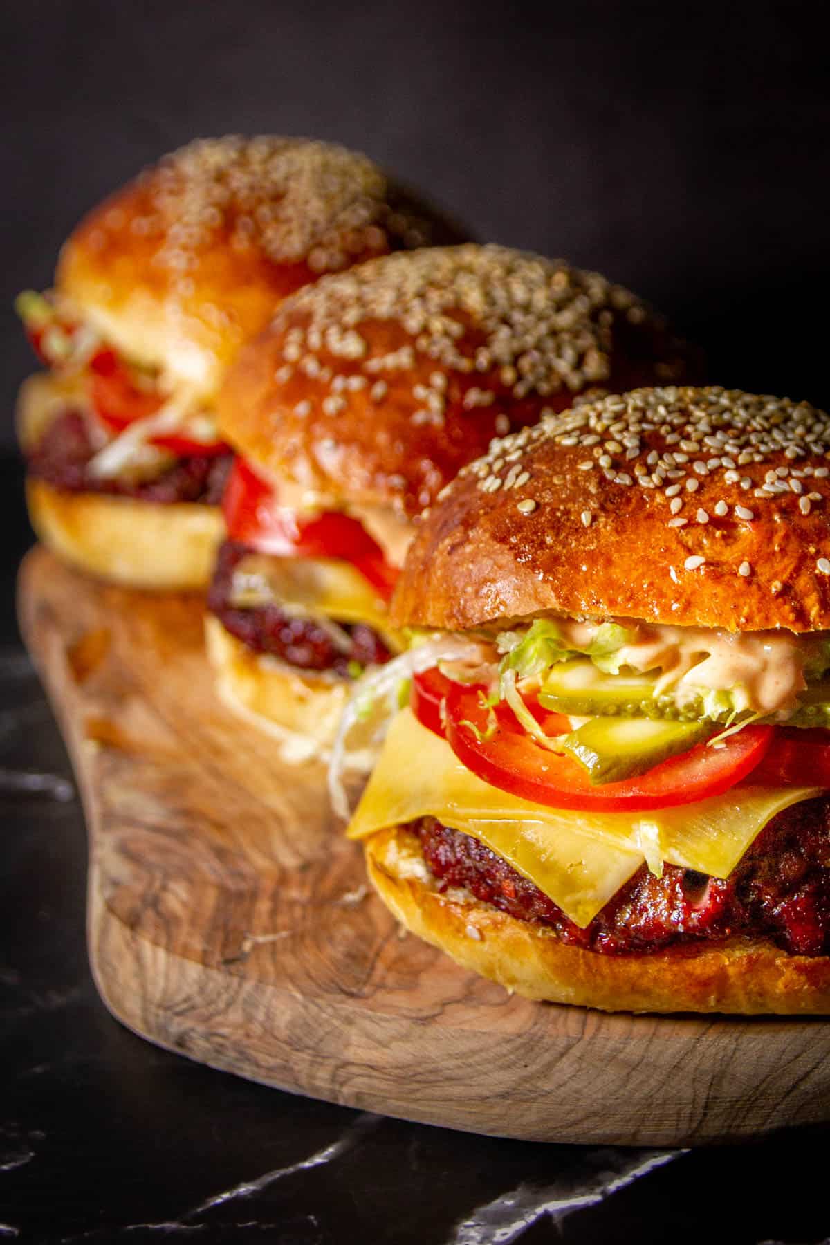 3 smoked burgers on a wooden board.