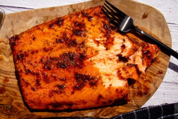 The finished hot smoked salmon on a wooden board with a fork pulling the flesh apart.