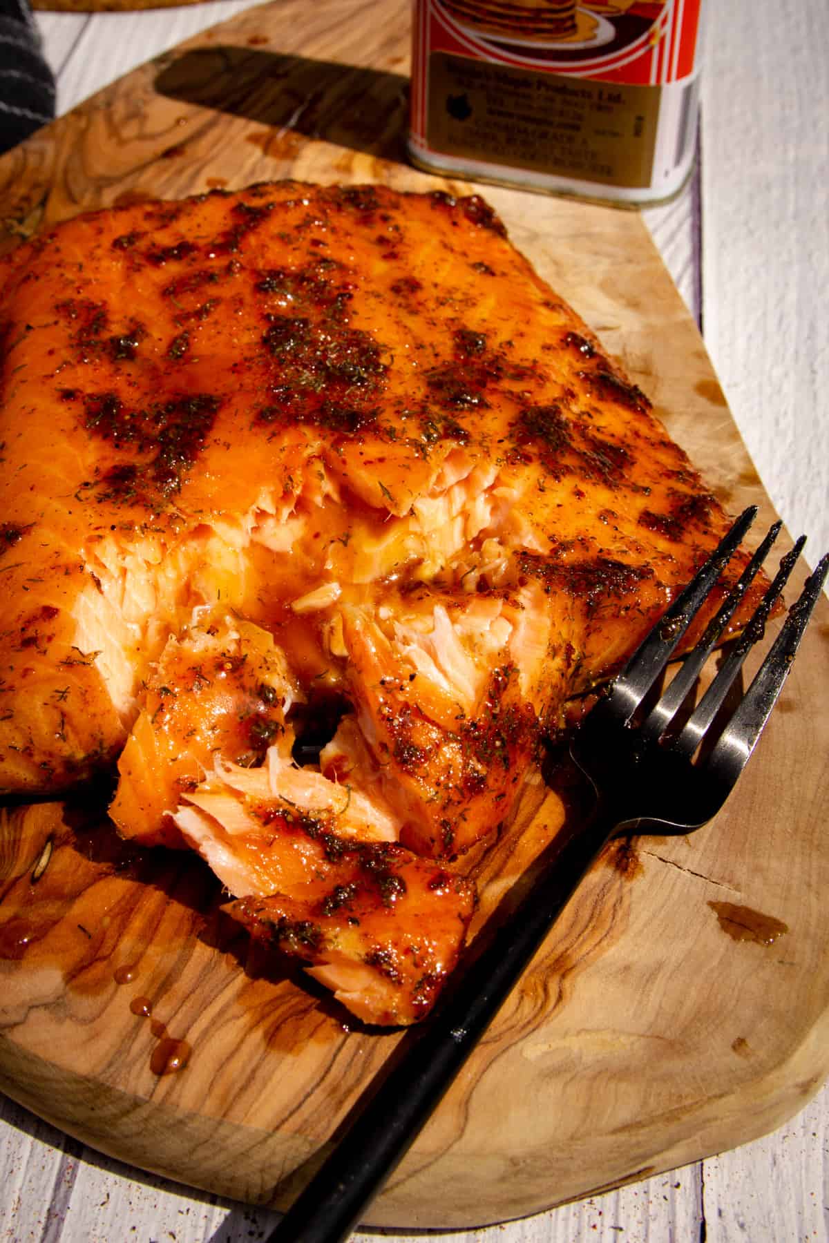 Maple glazed hot smoked traeger salmon on a wooden board with a fork flaking the flesh.